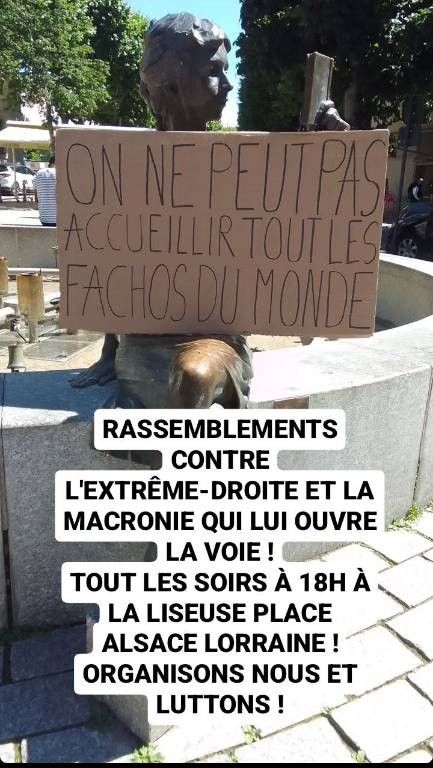 La statue grandeur nature d'une femme assise qui lit un livre, à laquelle on a rajouté une pancarte en carton « On ne peut pas acceillir tous les fachos du monde ».